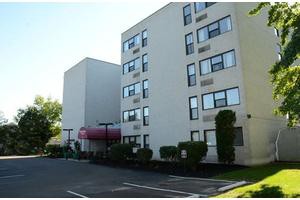 A multi-story residential apartment building with a parking lot and entrance canopy.