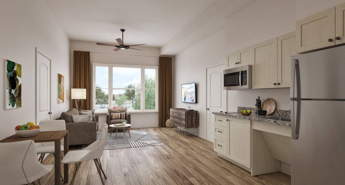 A modern apartment interior with a combined living room and kitchen, featuring wood flooring and ample natural light.