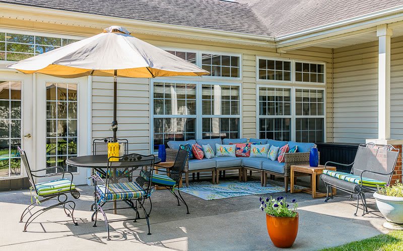 A cozy outdoor patio area featuring a sectional sofa with colorful cushions, a dining table with an umbrella, and a potted plant.