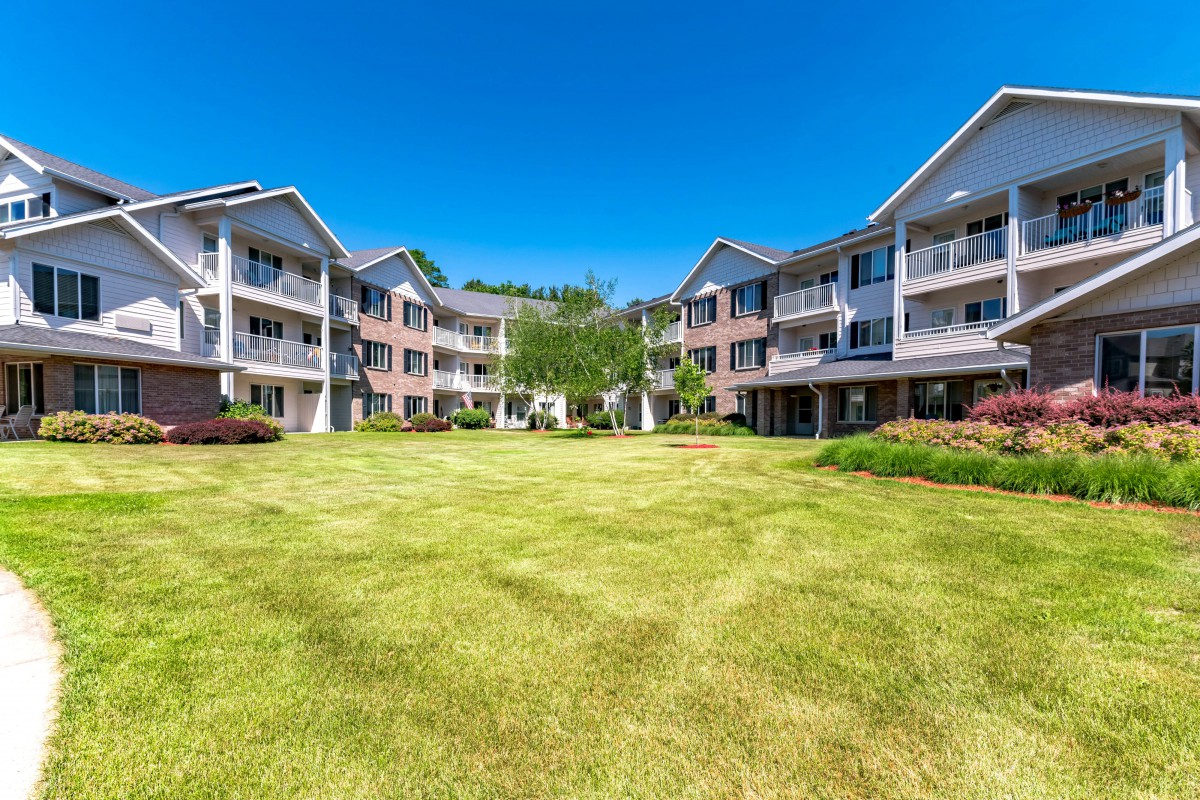 A residential apartment complex with a large grassy lawn, under a clear blue sky.