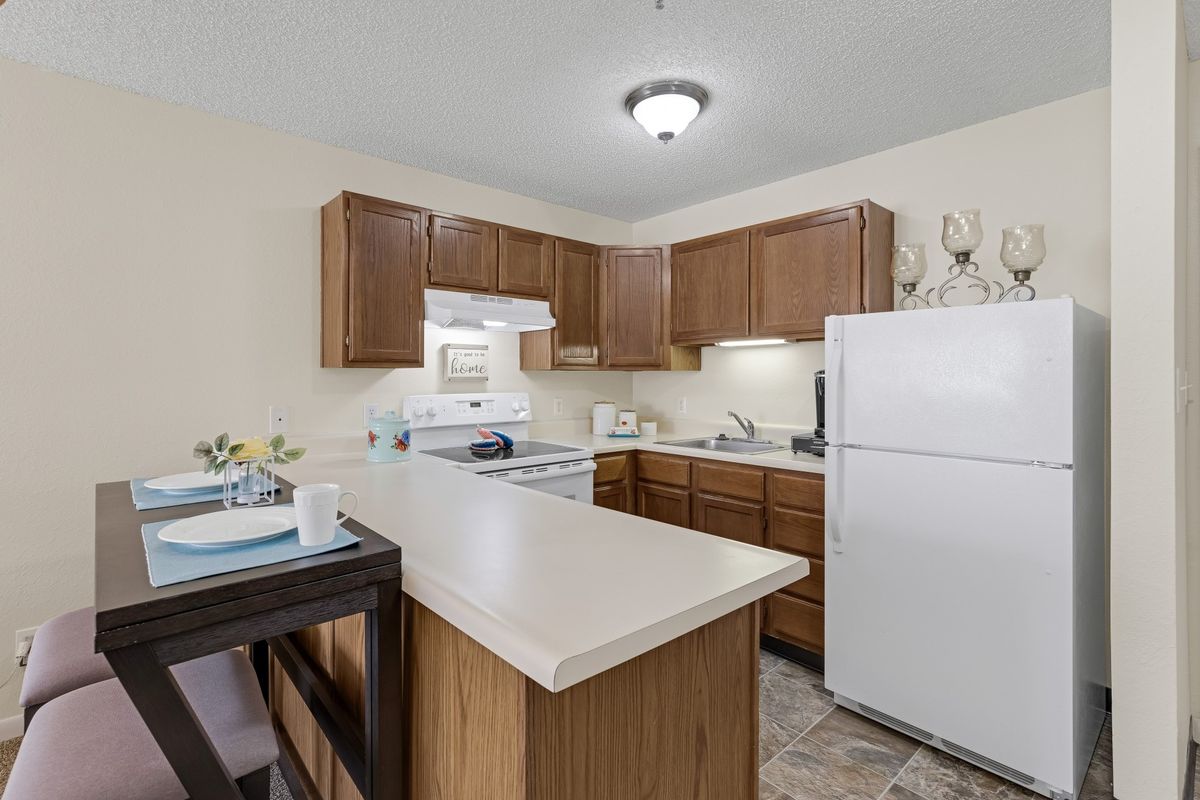 A modern kitchen with wood cabinets, an island counter, and standard appliances including a stove and refrigerator.