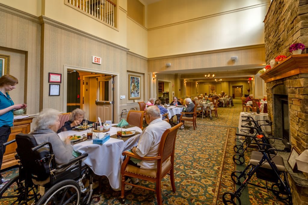 A dining area in a nursing home with residents gathered around tables.