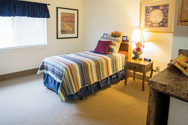A cozy bedroom with a single bed featuring striped bedding, accompanied by a nightstand and lamp.