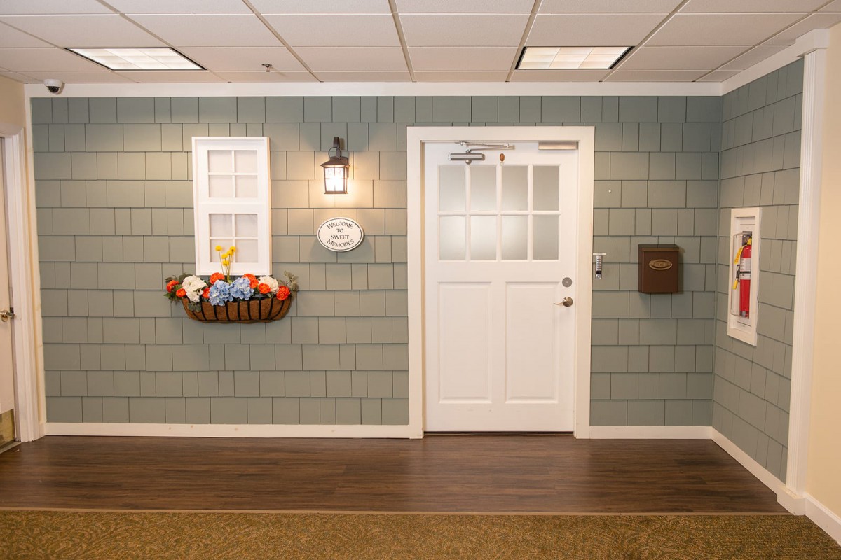 A welcoming interior setup featuring a door and window, accented with a basket of artificial flowers and a wall-mounted lamp.