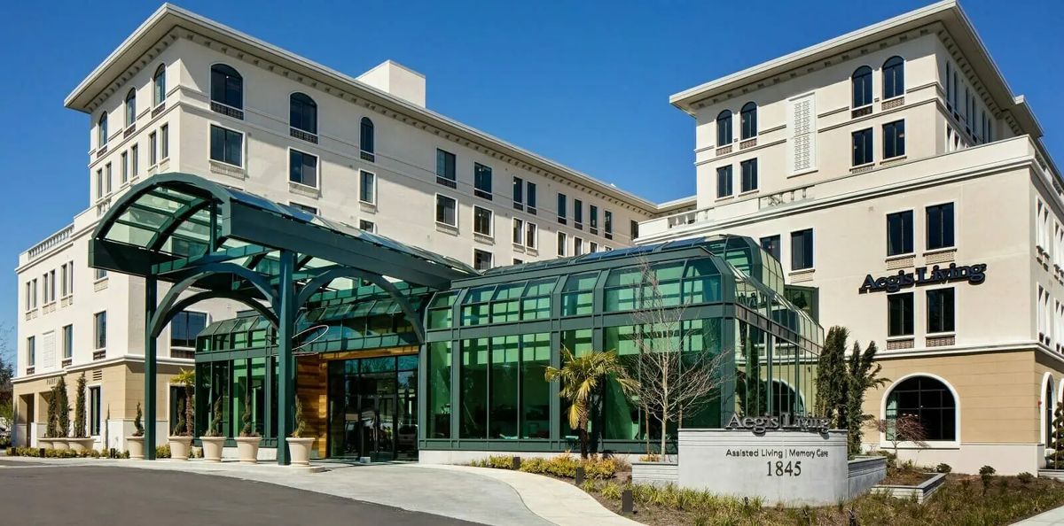 A modern hospital building featuring a glass entrance structure under a clear blue sky.