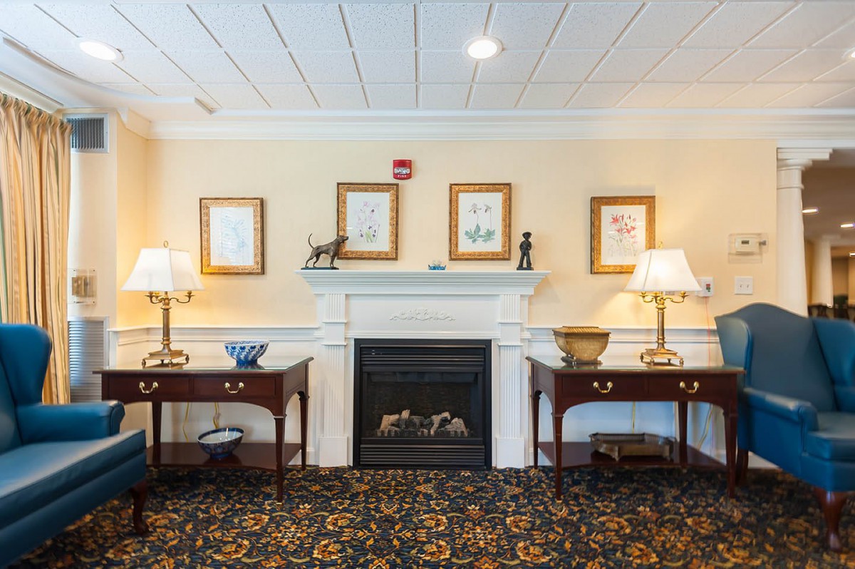 A cozy living room with a central fireplace flanked by two tables and lamps, adorned with framed artwork on the wall.