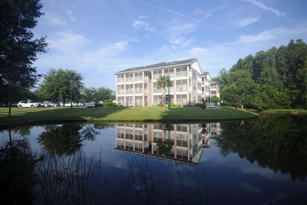 A serene view of a white building reflected in a calm pond surrounded by greenery.