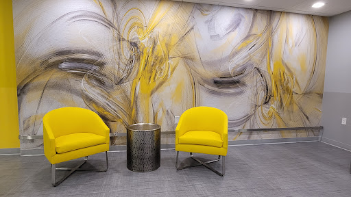 A modern waiting area featuring bright yellow chairs, a metallic table, and an abstract wall mural.