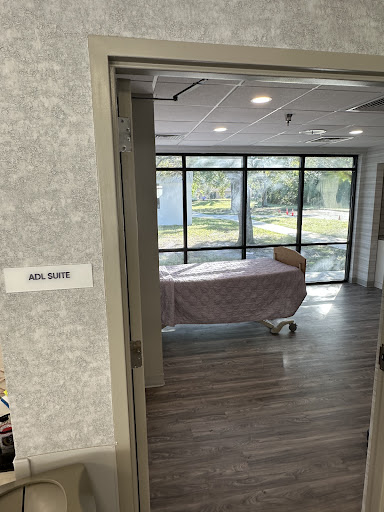 A view into a hospital patient room featuring a bed and large windows providing natural light.
