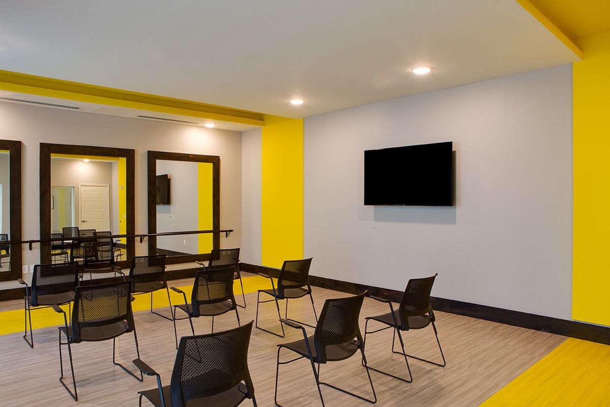 A modern conference room featuring chairs arranged in rows, a wall-mounted television, and large mirrors.
