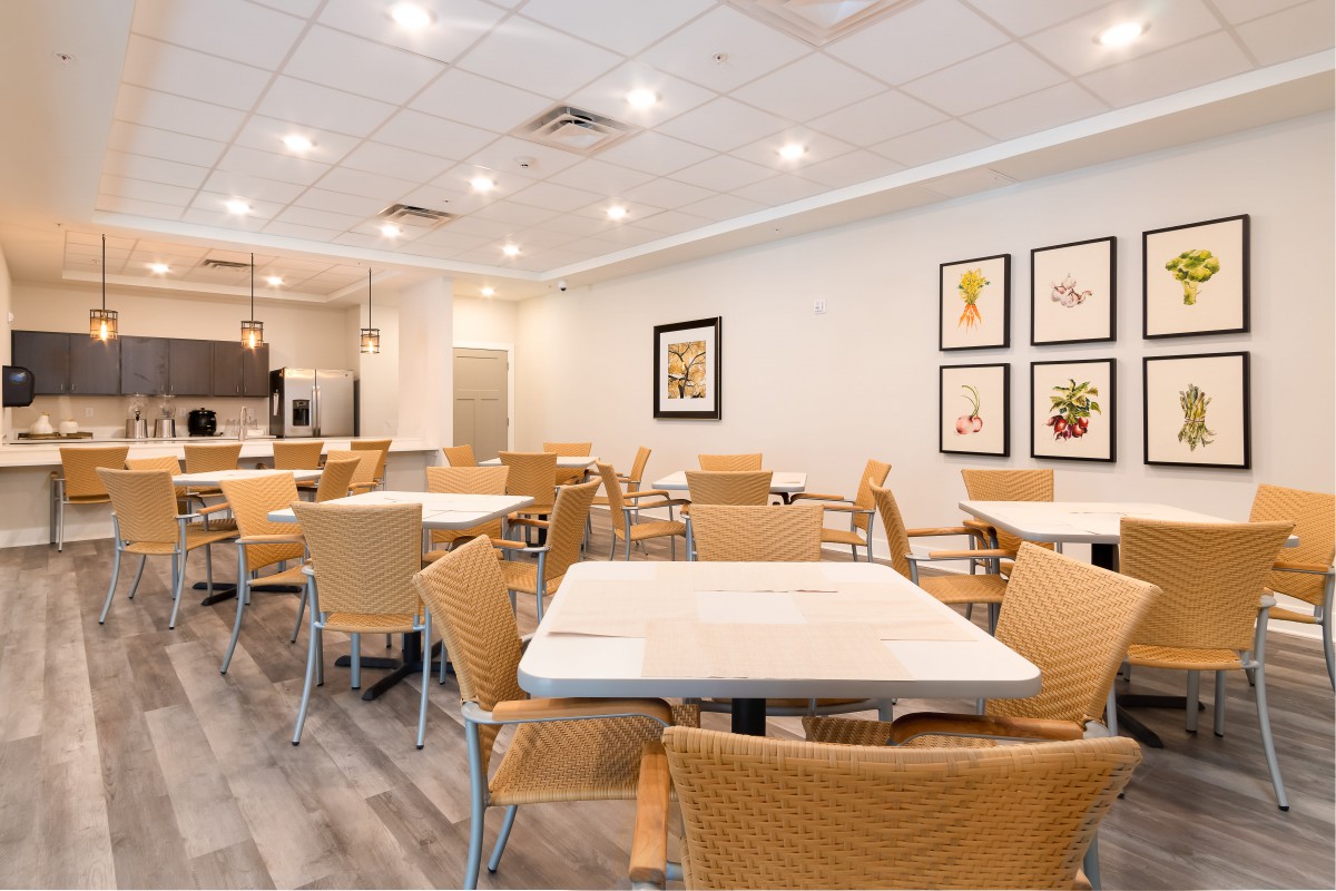 A modern cafeteria with neatly arranged tables and chairs, bright lighting, and decorative artwork on the walls.