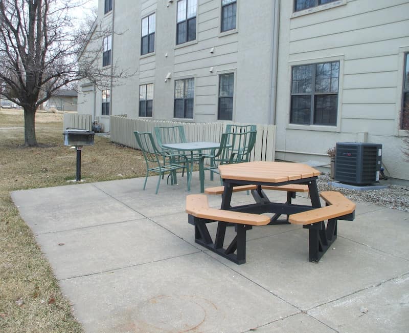 An outdoor patio area with a picnic table, chairs, and a grill next to a building.