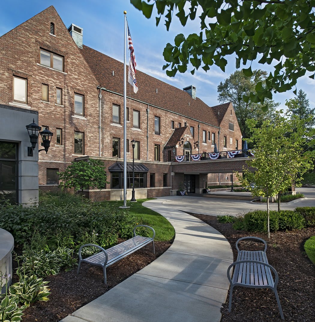 A brick building with a sloped roof, surrounded by greenery and benches along a winding pathway.