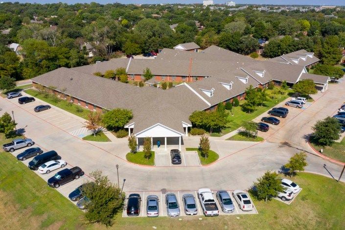 Aerial view of a building with a surrounding parking lot and cars in a suburban area.