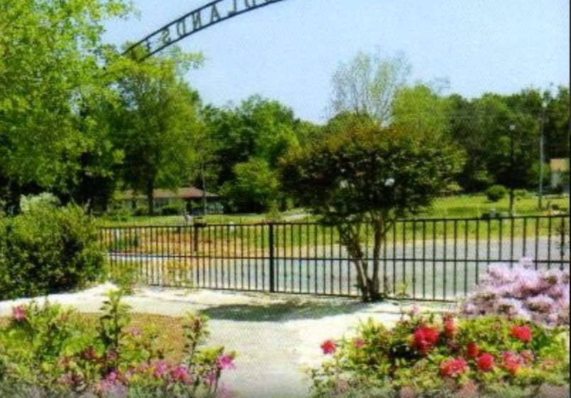 A scenic view of a garden with colorful flowers, a black fence, and lush green trees in the background.