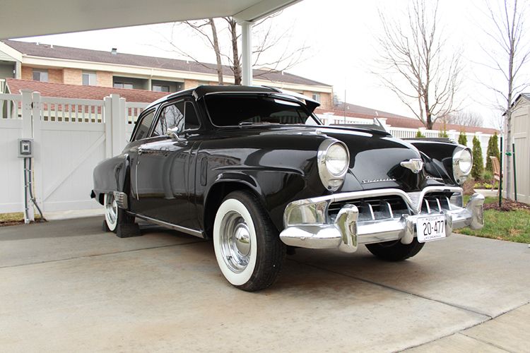A vintage black classic car with whitewall tires parked in a residential area.
