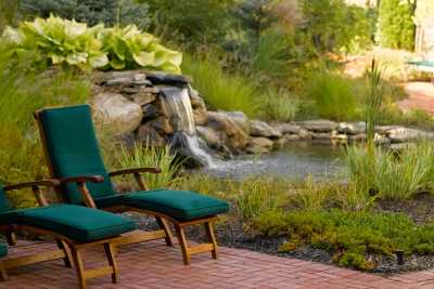 A tranquil garden scene with chairs overlooking a small waterfall and pond.