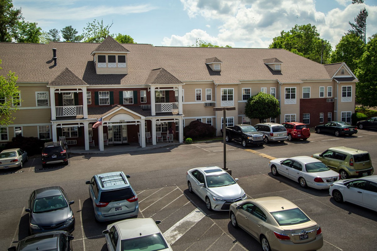 A residential building with a parking lot filled with cars on a sunny day.
