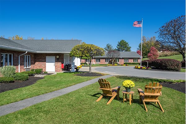 A peaceful motel courtyard with chairs and a table set on a grassy lawn, featuring manicured landscaping and a flag flying high.
