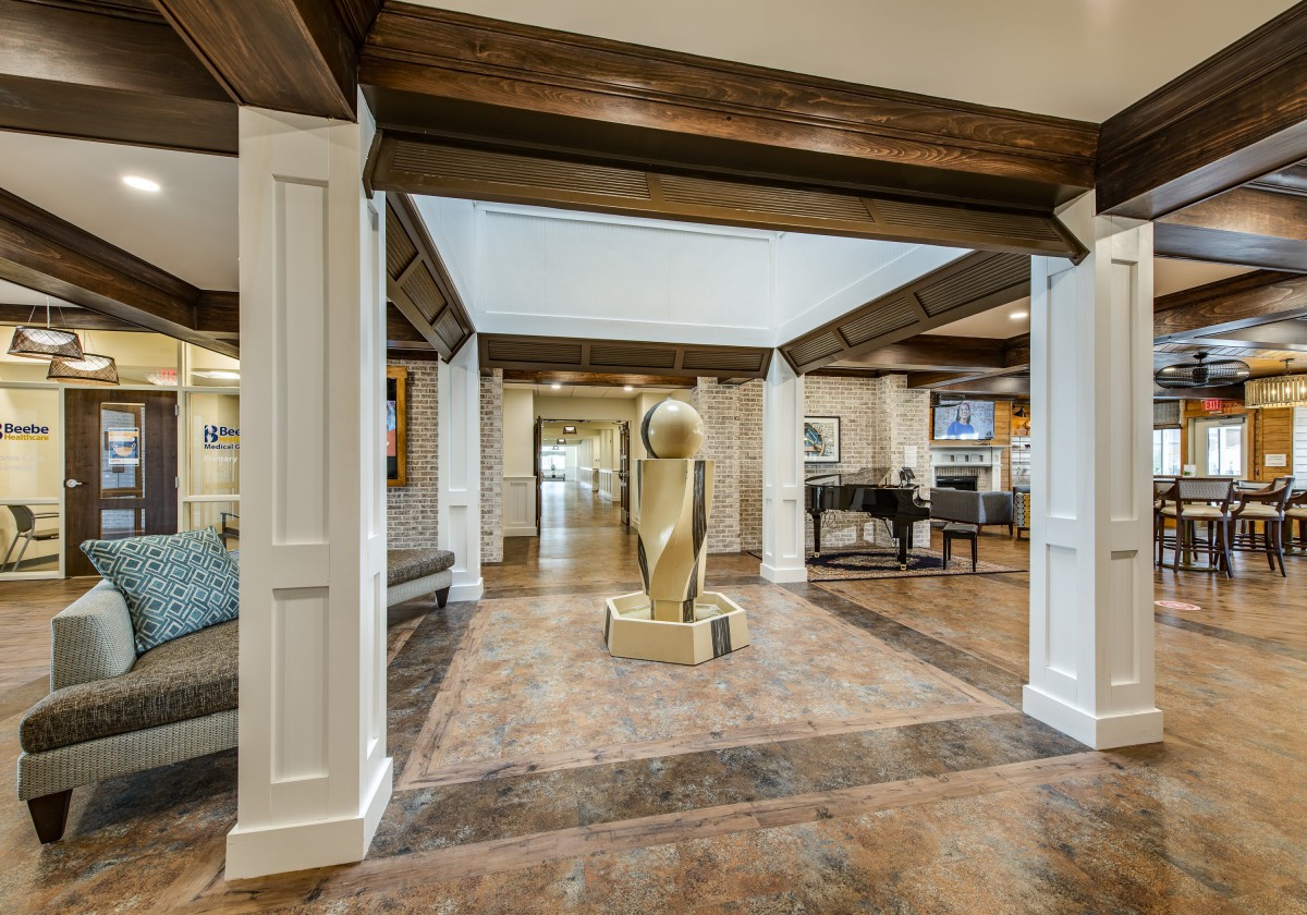 A stylish lobby featuring a central sculpture, wood beams, and a grand piano.