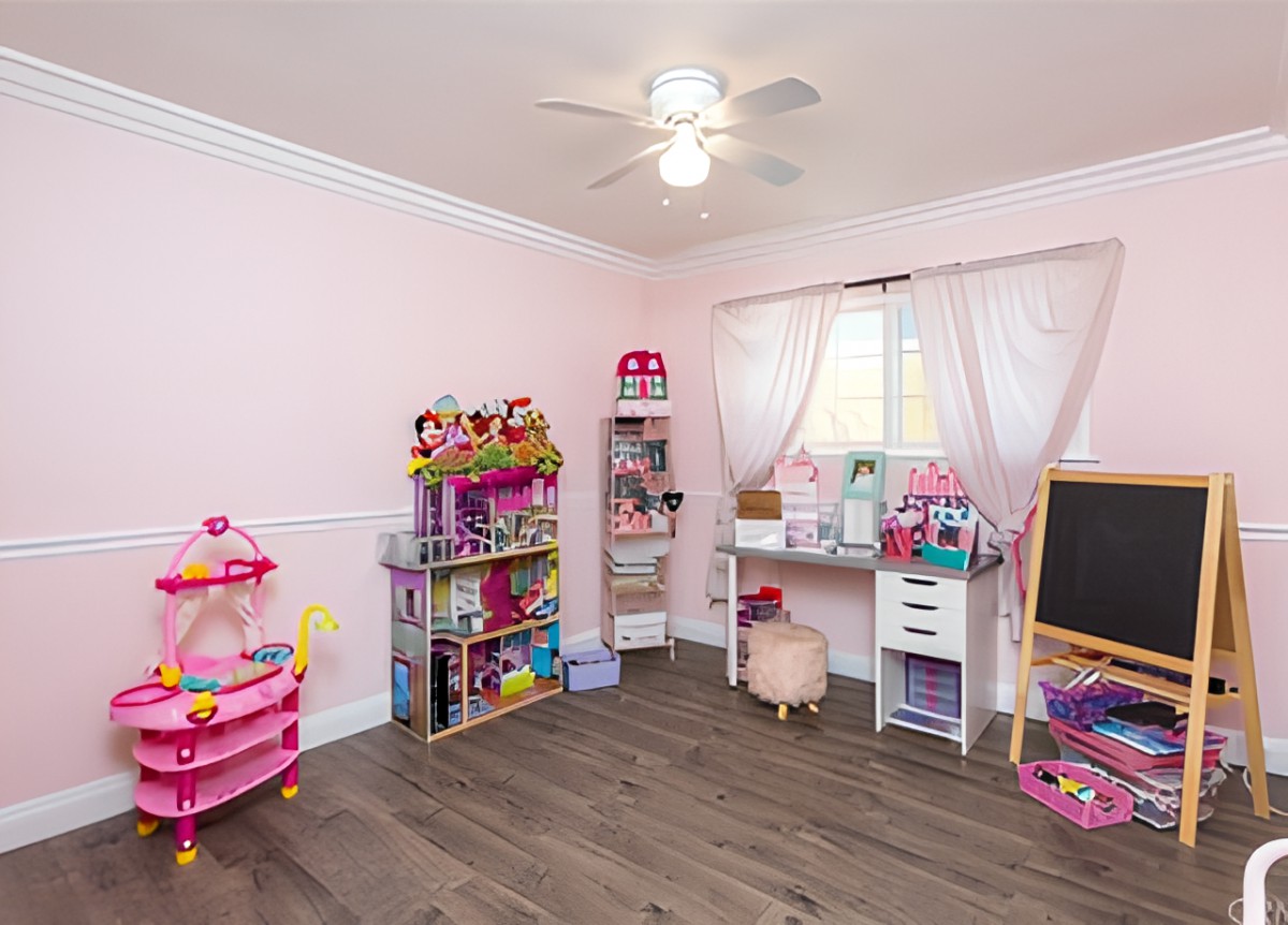 A neatly organized children's playroom featuring pink walls and a variety of toys on shelves and a desk.