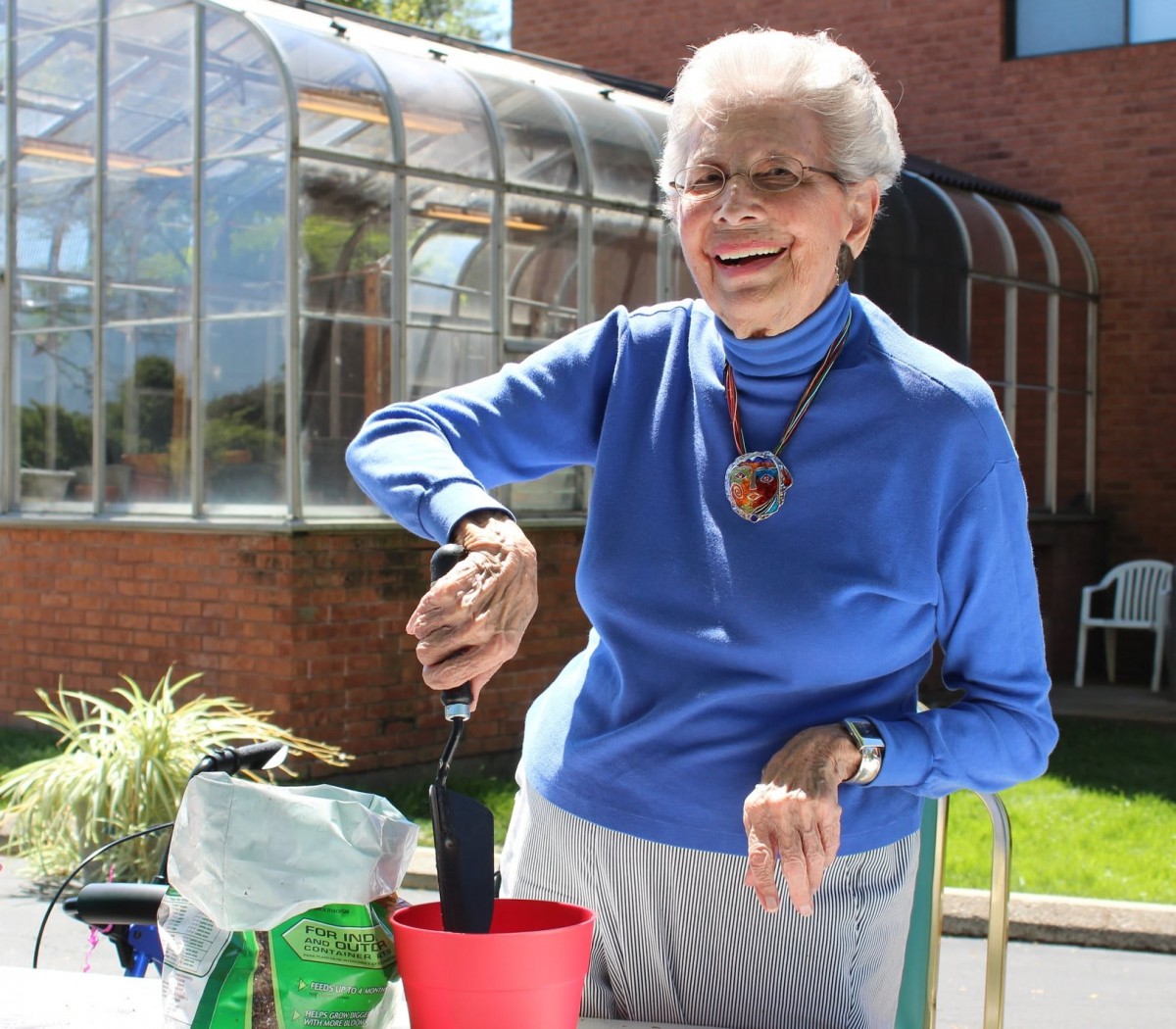 An elderly woman happily gardening outside on a sunny day.