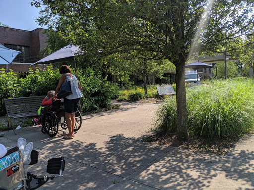 A caregiver pushes a wheelchair-bound person along a scenic path in a park.