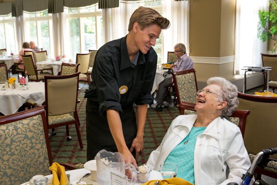 A waiter shares a laugh with an elderly woman at a dining area.