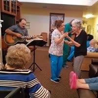 Elderly residents enjoying live music and dancing in a cozy common area.