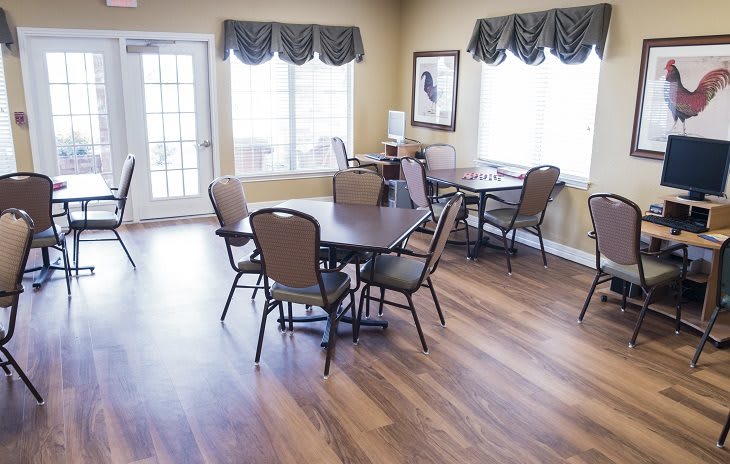 A bright dining area with tables and chairs, featuring hardwood floors and large windows.