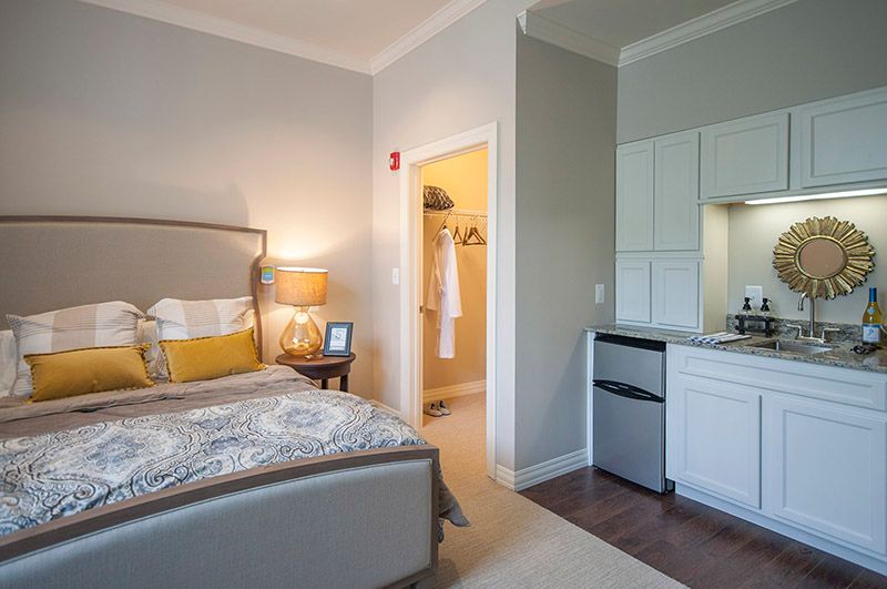 A cozy bedroom with a modern design, featuring a comfortable bed, nightstand with a lamp, and a small kitchenette.