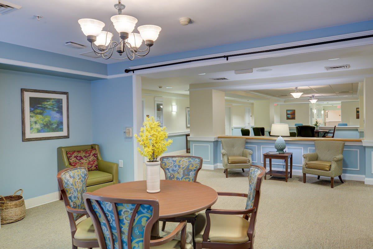 A cozy living and dining area featuring comfortable seating, a wooden table, and a chandelier under soft blue walls.