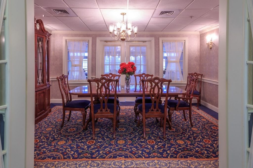 A formal dining room with an elegant wooden table and chairs, a chandelier overhead, and decorative flowers on the table.