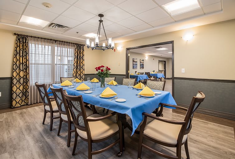 A dining room with a large table set for guests, featuring a blue tablecloth and decorative napkins.