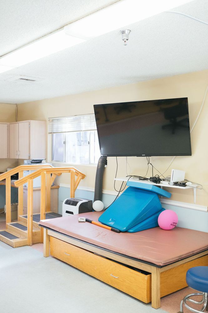 A rehabilitation room equipped with therapy tools, including a TV, exercise balls, and wooden stairs.