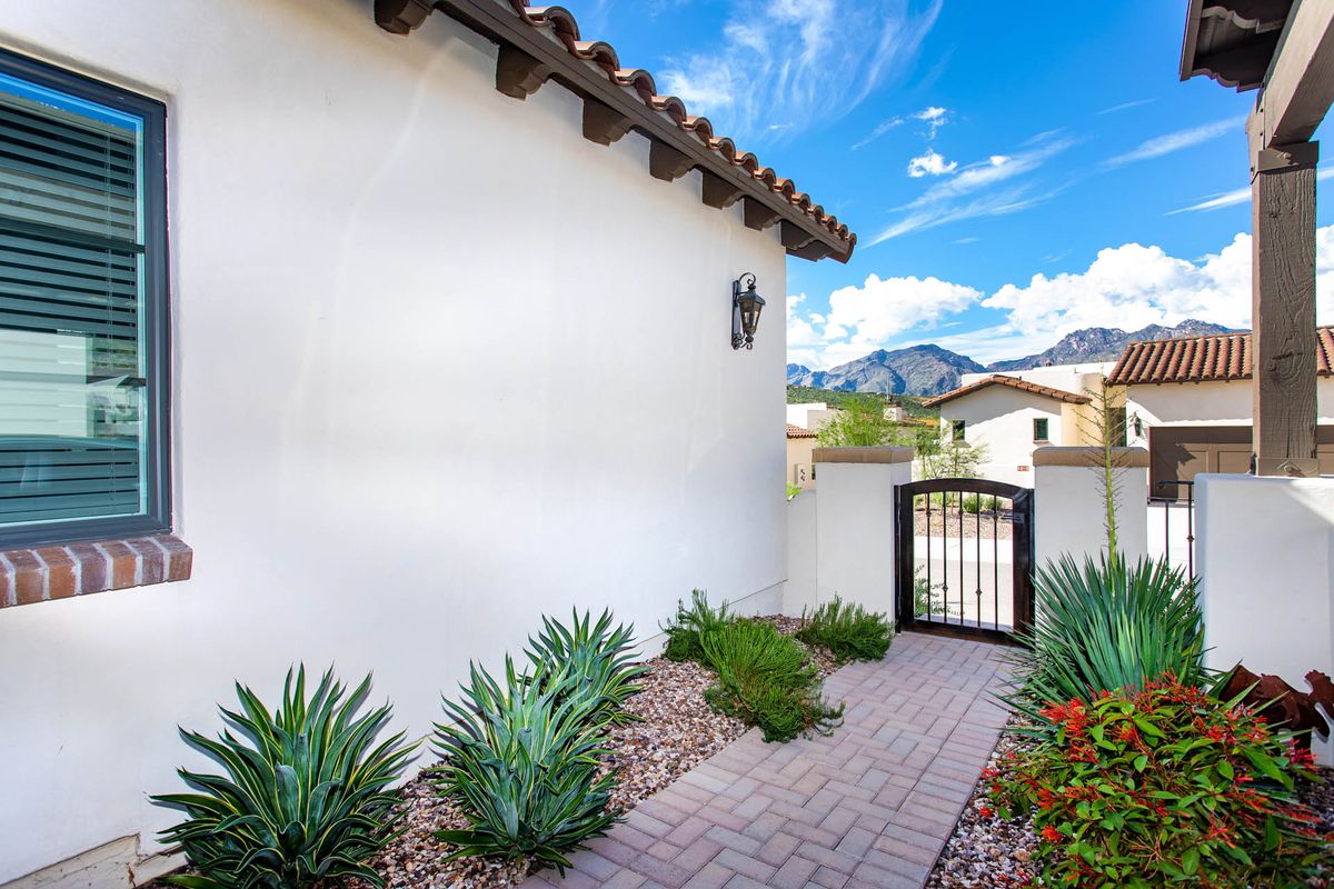 A charming desert garden pathway leading to a wrought iron gate, with mountainous views in the background.