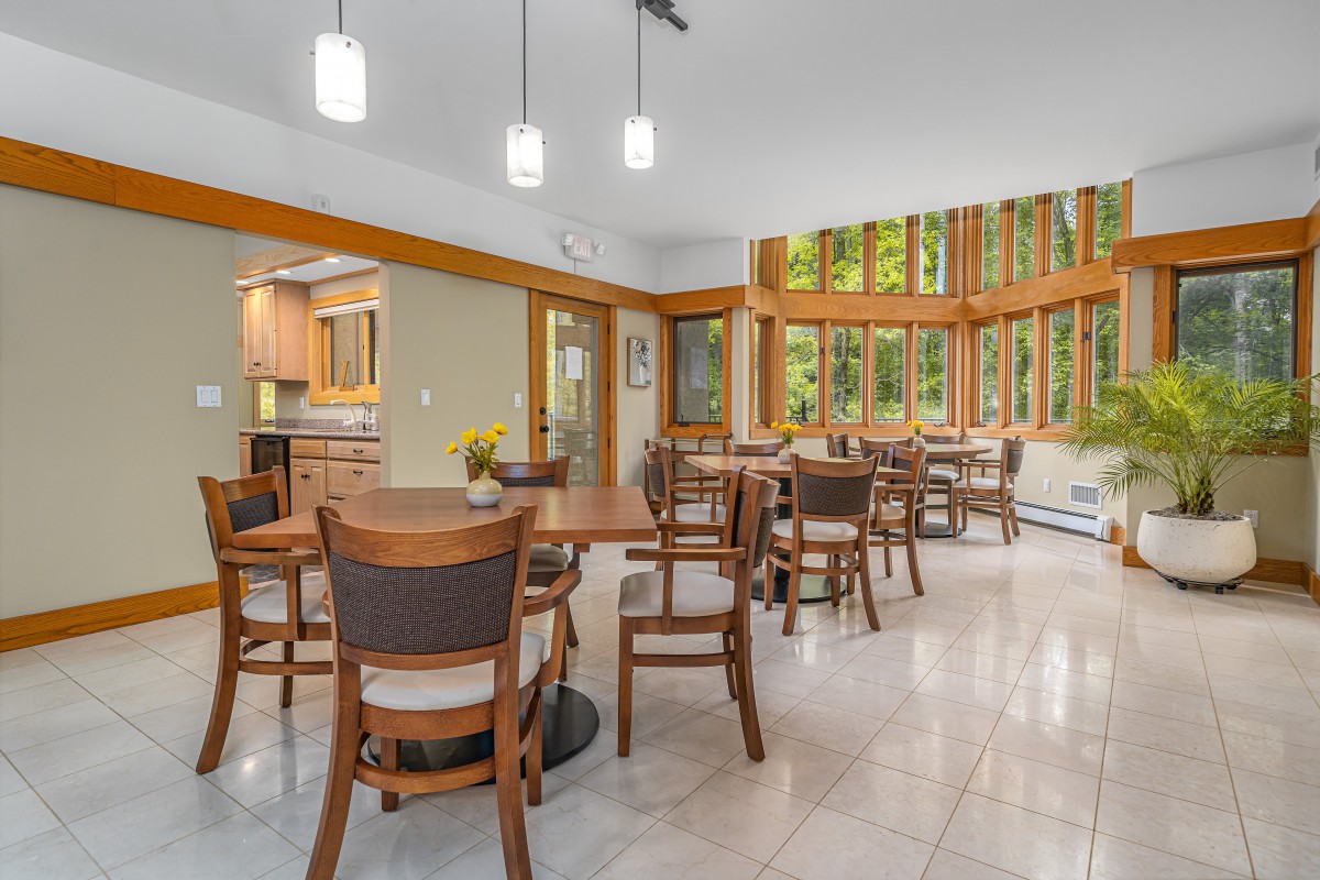 A modern dining area with wooden furniture and large windows overlooking a lush green view.