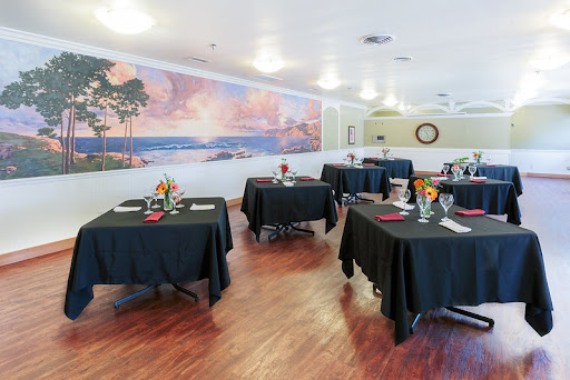 A cozy restaurant setting featuring tables adorned with black tablecloths and decorative centerpieces, complemented by a beautiful mural on the wall.