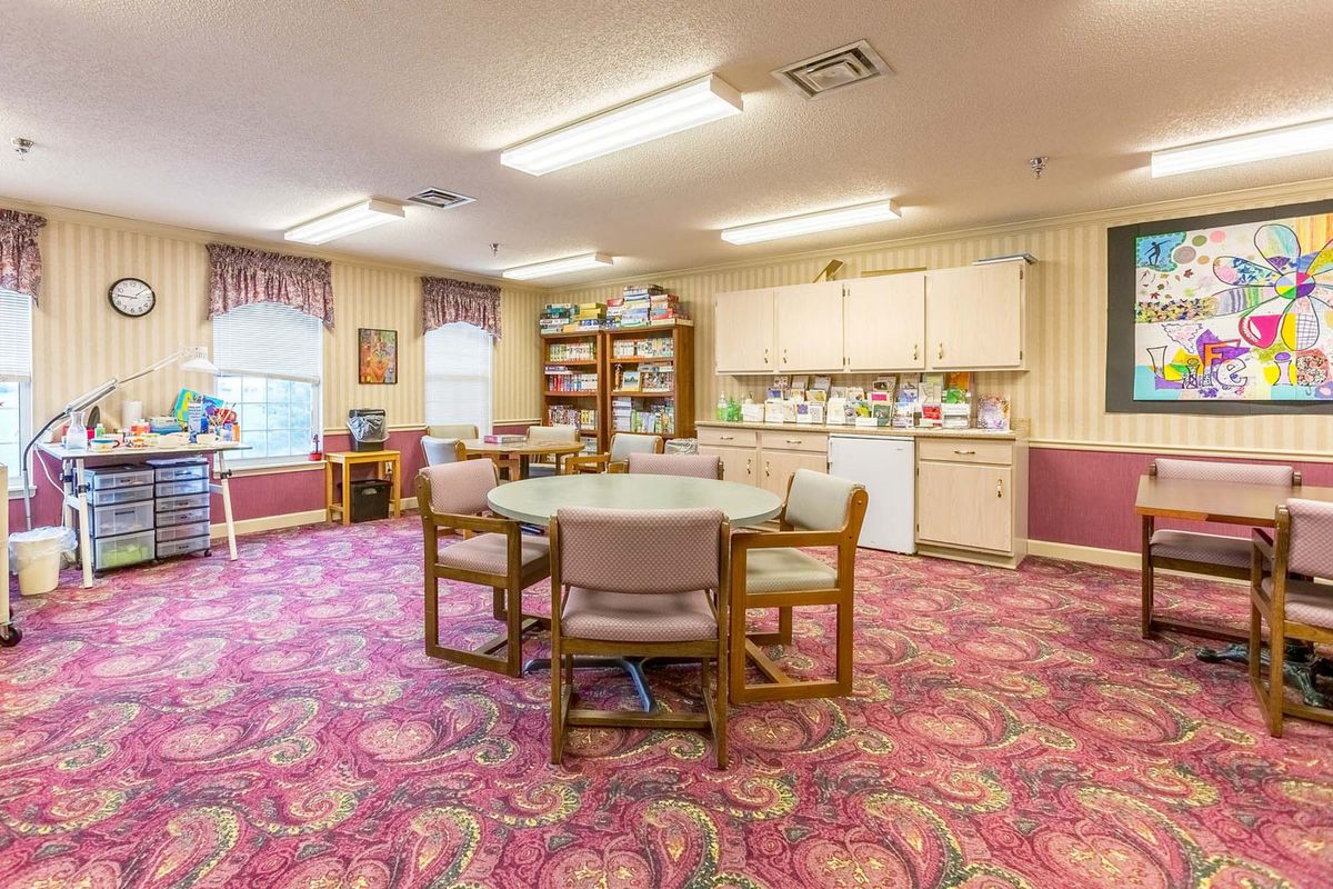 A cozy interior room featuring a round table with chairs, surrounded by bookshelves and a small kitchen area.