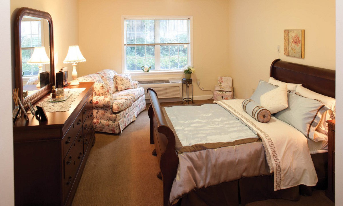 A cozy bedroom with a bed, sofa, and a window letting in natural light.