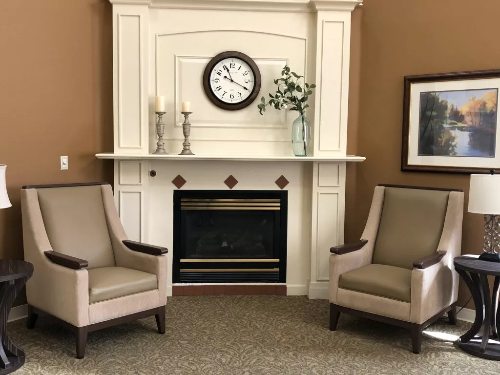 A cozy living room setting featuring a fireplace with two armchairs and a clock above the mantelpiece.