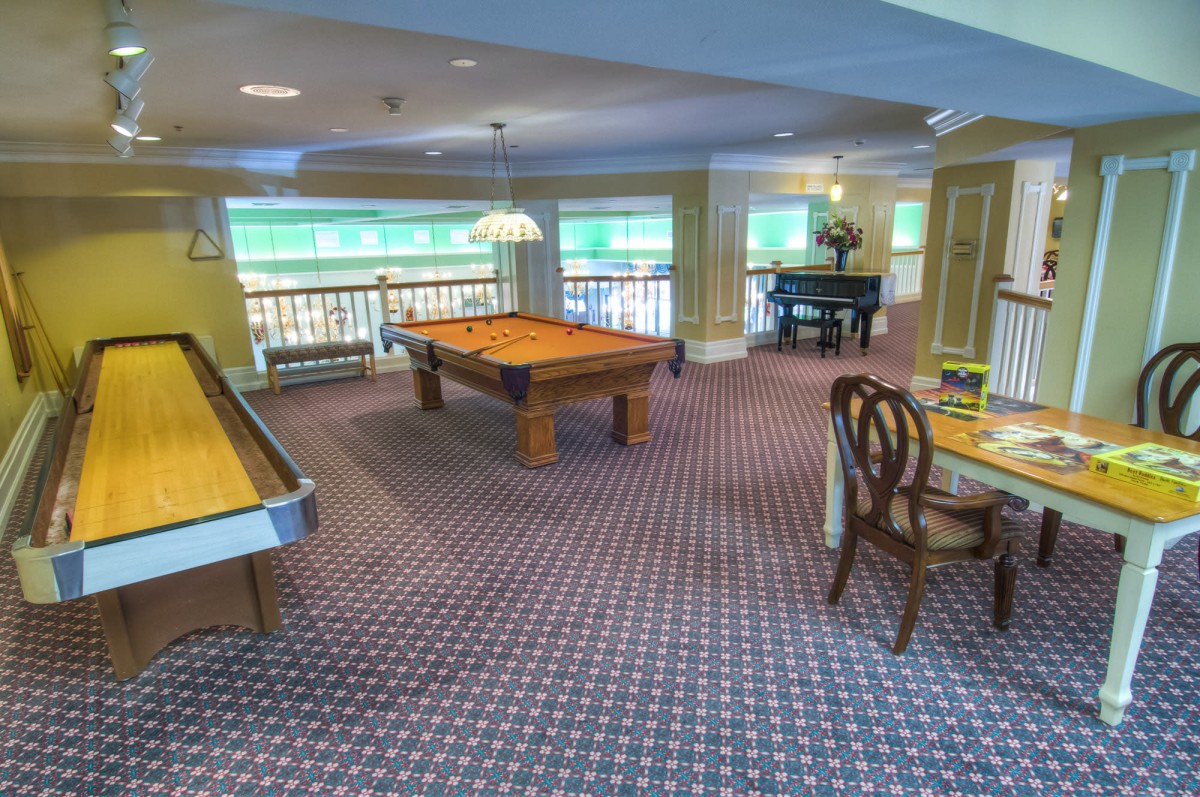 A spacious game room featuring a pool table, shuffleboard, and seating area.