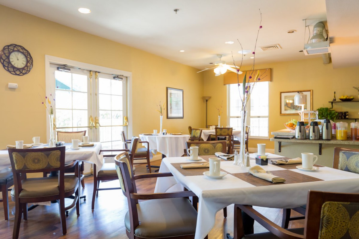 A cozy dining area with neatly arranged tables and chairs, featuring large windows that let in ample natural light.
