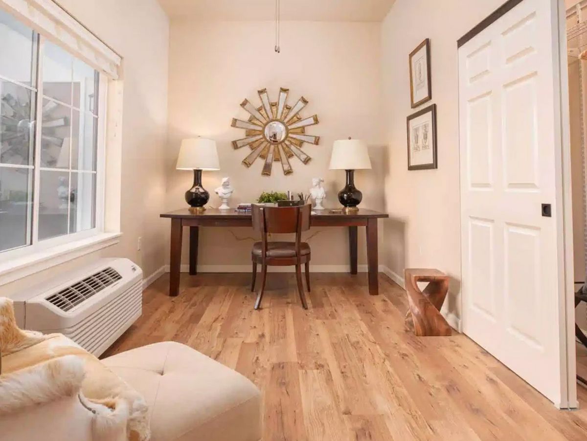 A cozy home office featuring wooden flooring, a decorative mirror, and minimalist furnishings.