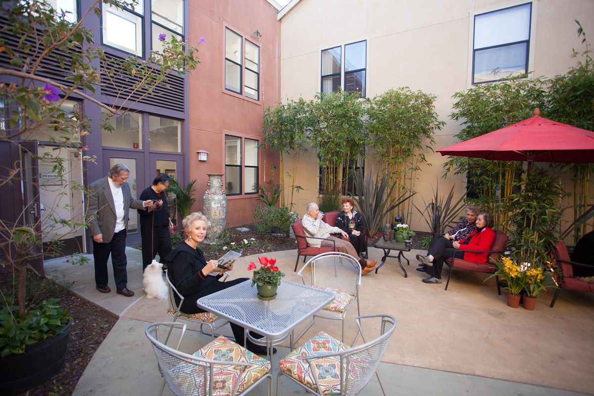 A group of people enjoying a gathering on a cozy outdoor patio with seating and a red umbrella.