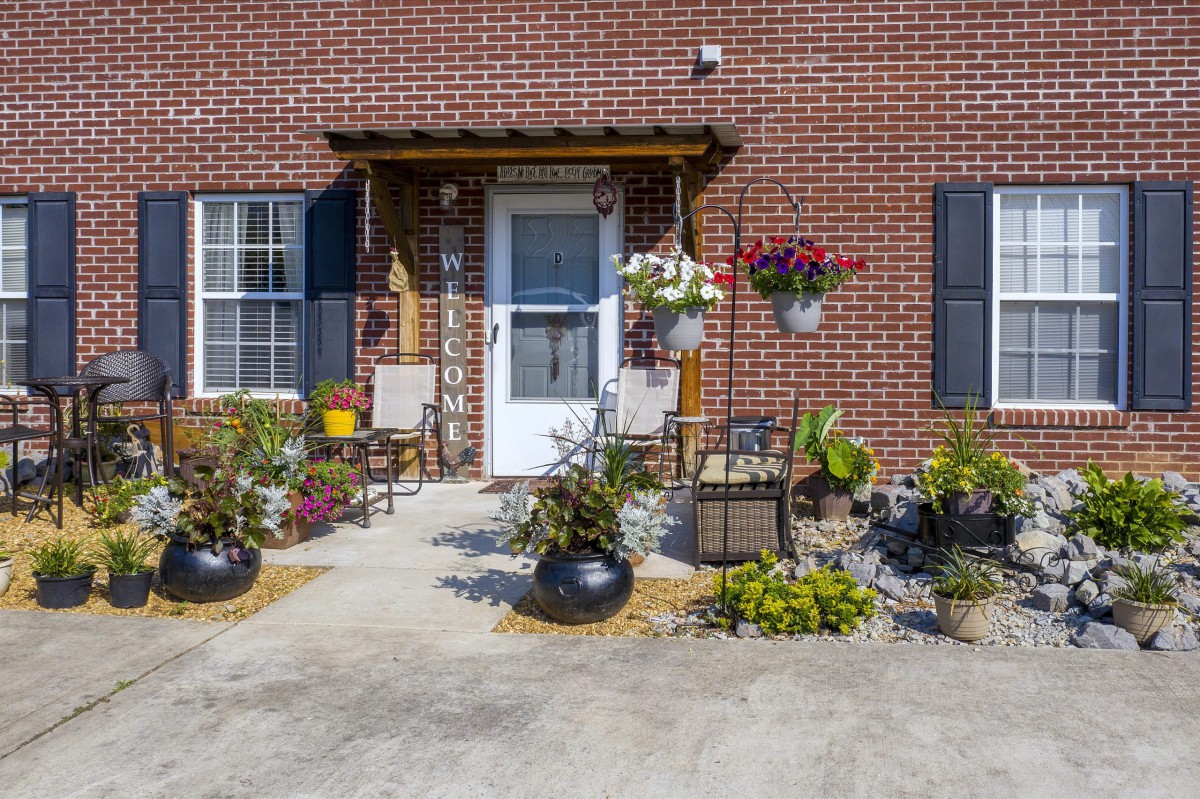A welcoming front porch with potted plants and outdoor seating against a brick wall.