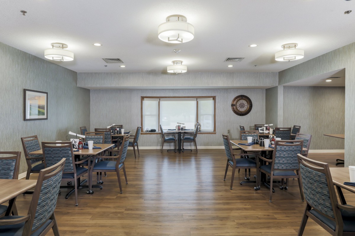 A spacious dining room with neatly arranged tables and chairs, featuring wooden floors and ample lighting.