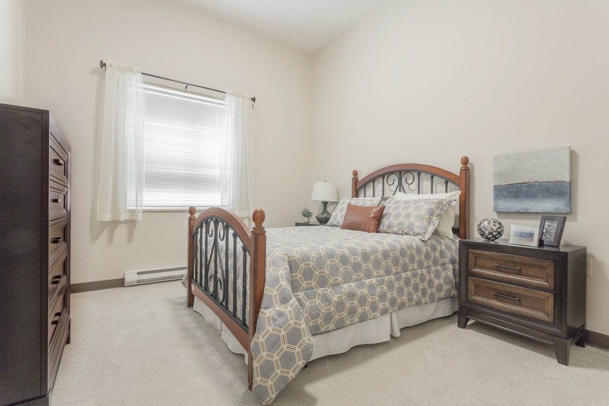 A cozy bedroom featuring a wooden bed, patterned bedding, and a bedside table with a lamp.