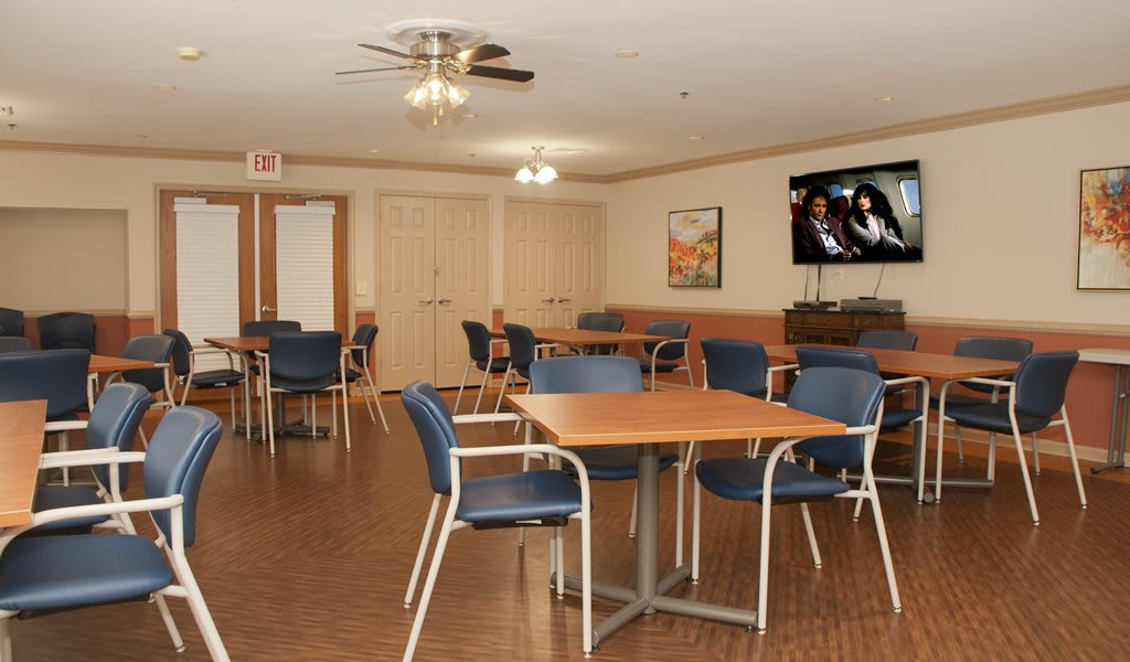 A community dining area with tables, chairs, and a television on the wall.