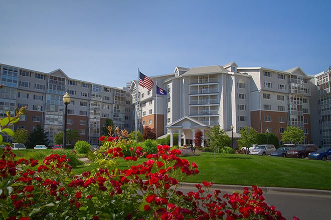 A residential building surrounded by a garden with red flowers and flags waving in front.